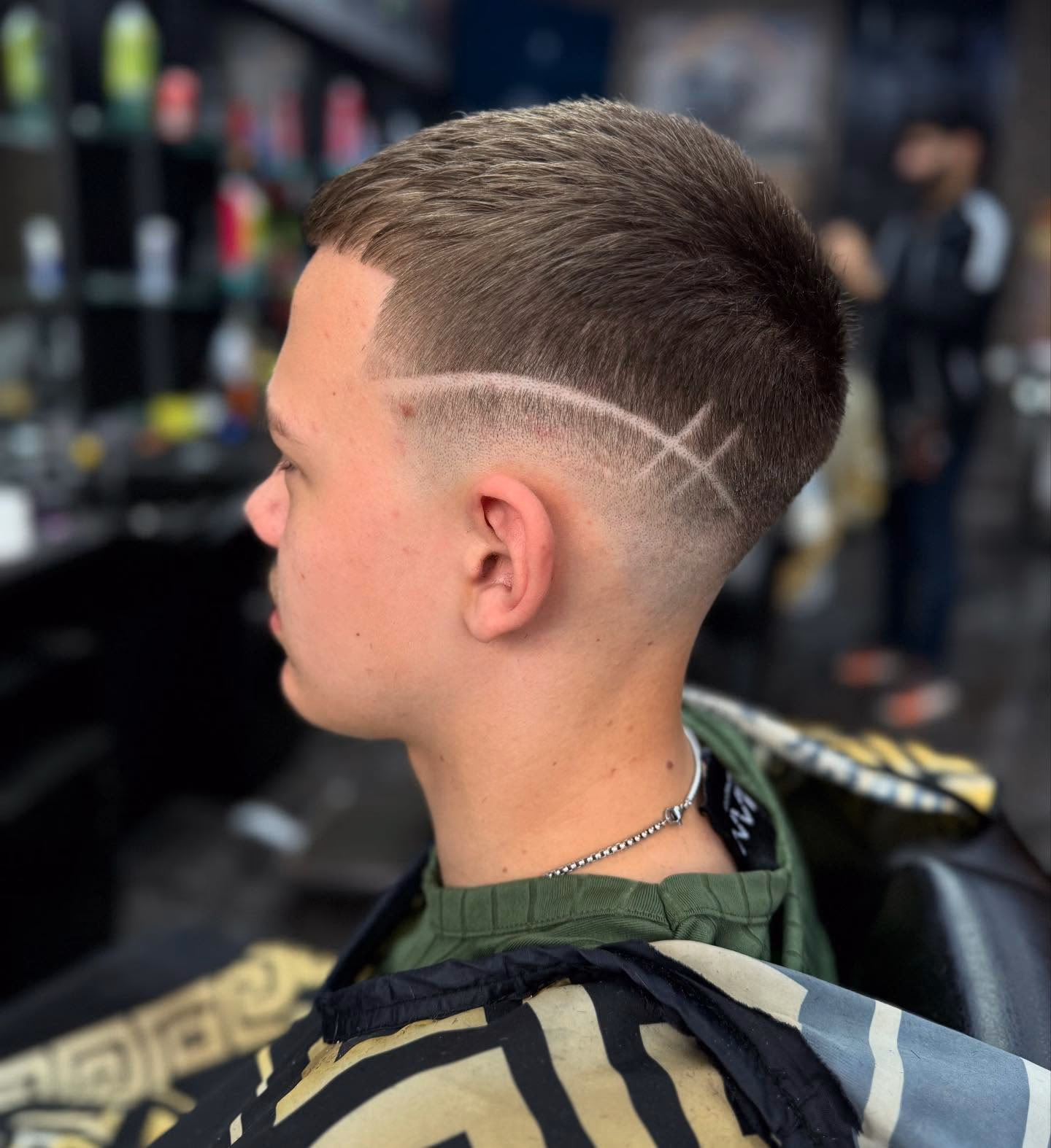 Short crop with a blunt fringe, high skin fade and a crossed double line shaved into the side, side profile