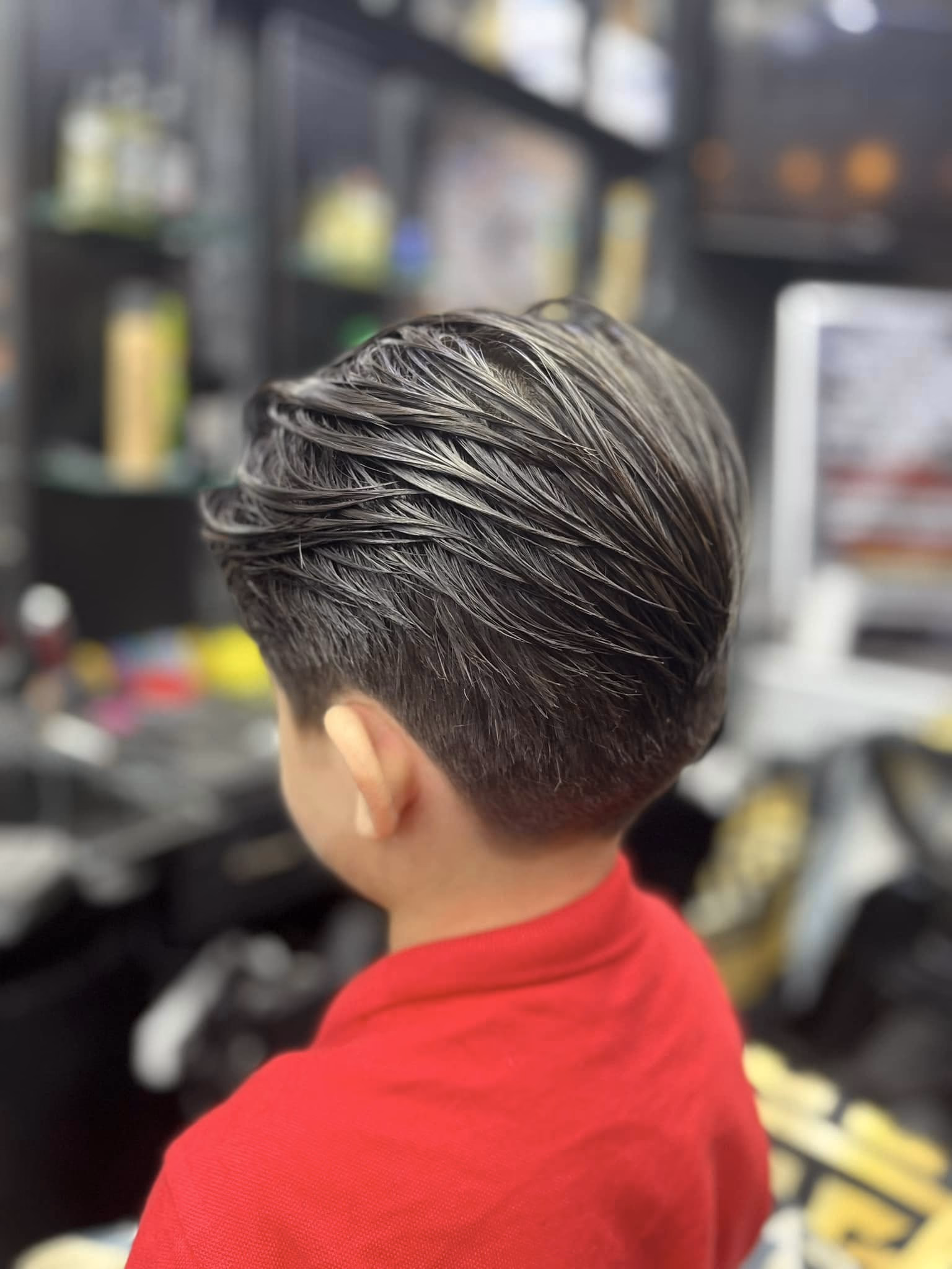 Dark hair combed back into a textured slick-back over a short tapered back, rear three-quarter view