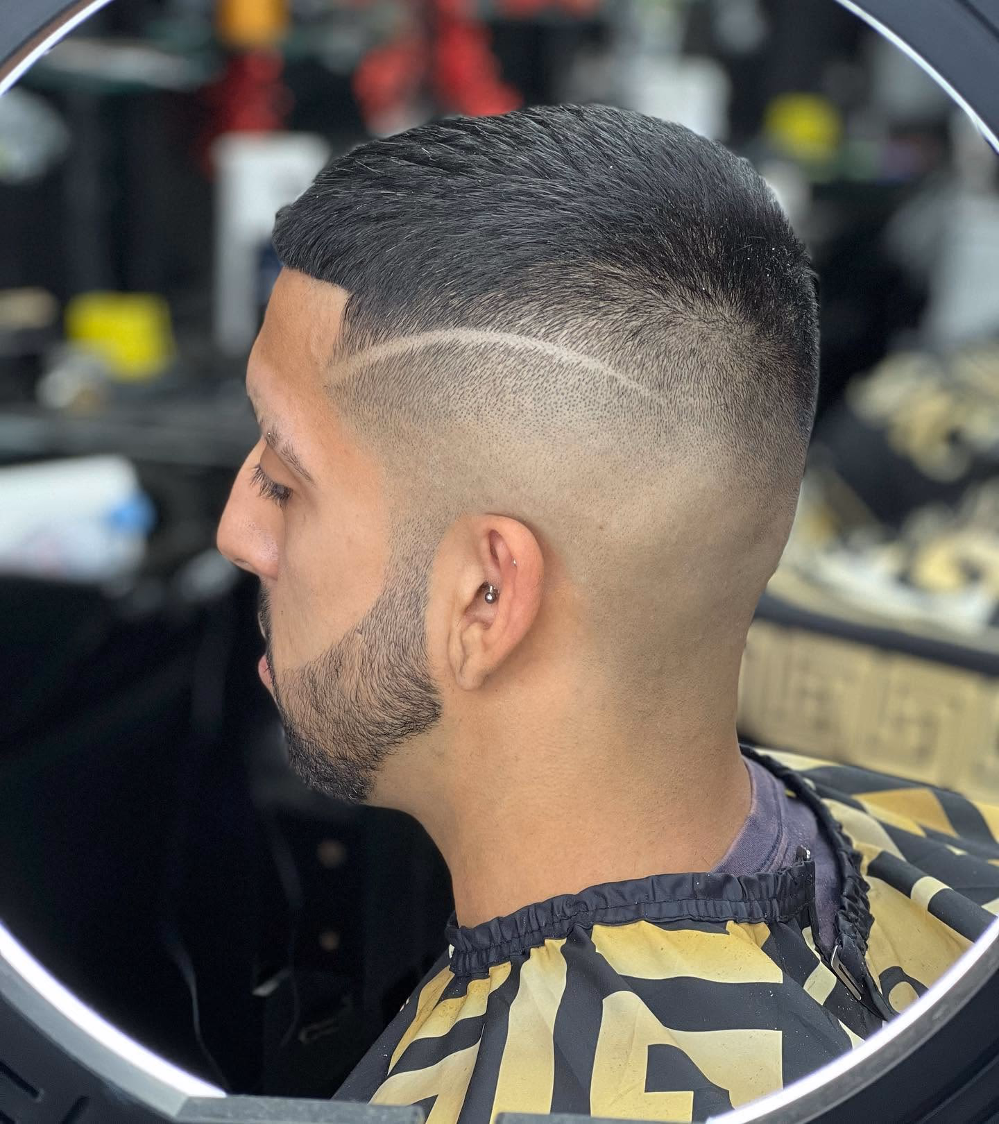 High skin fade with a shaved parting line cut into the side, brushed-back top and a beard tapered into the fade, side profile