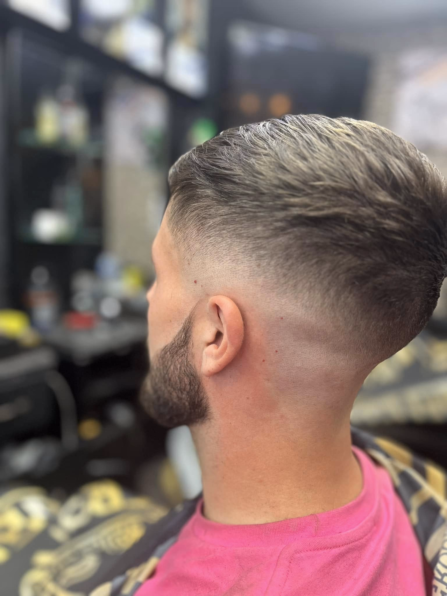 Mid skin fade with the top swept straight back and a full beard tapered along the jaw, side profile