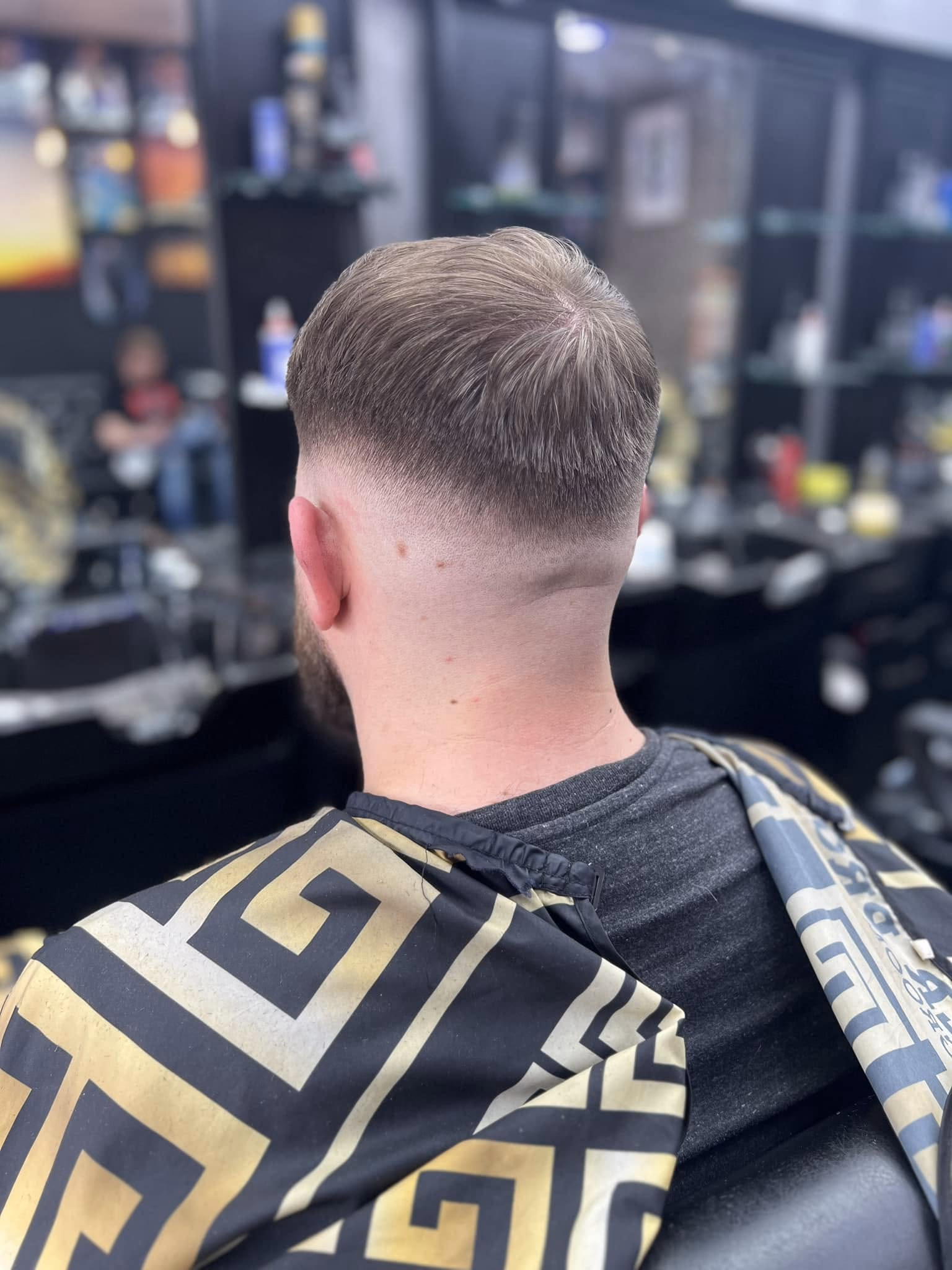 Low taper fade with the top combed straight back and a beard blended at the sideburn, seen from behind