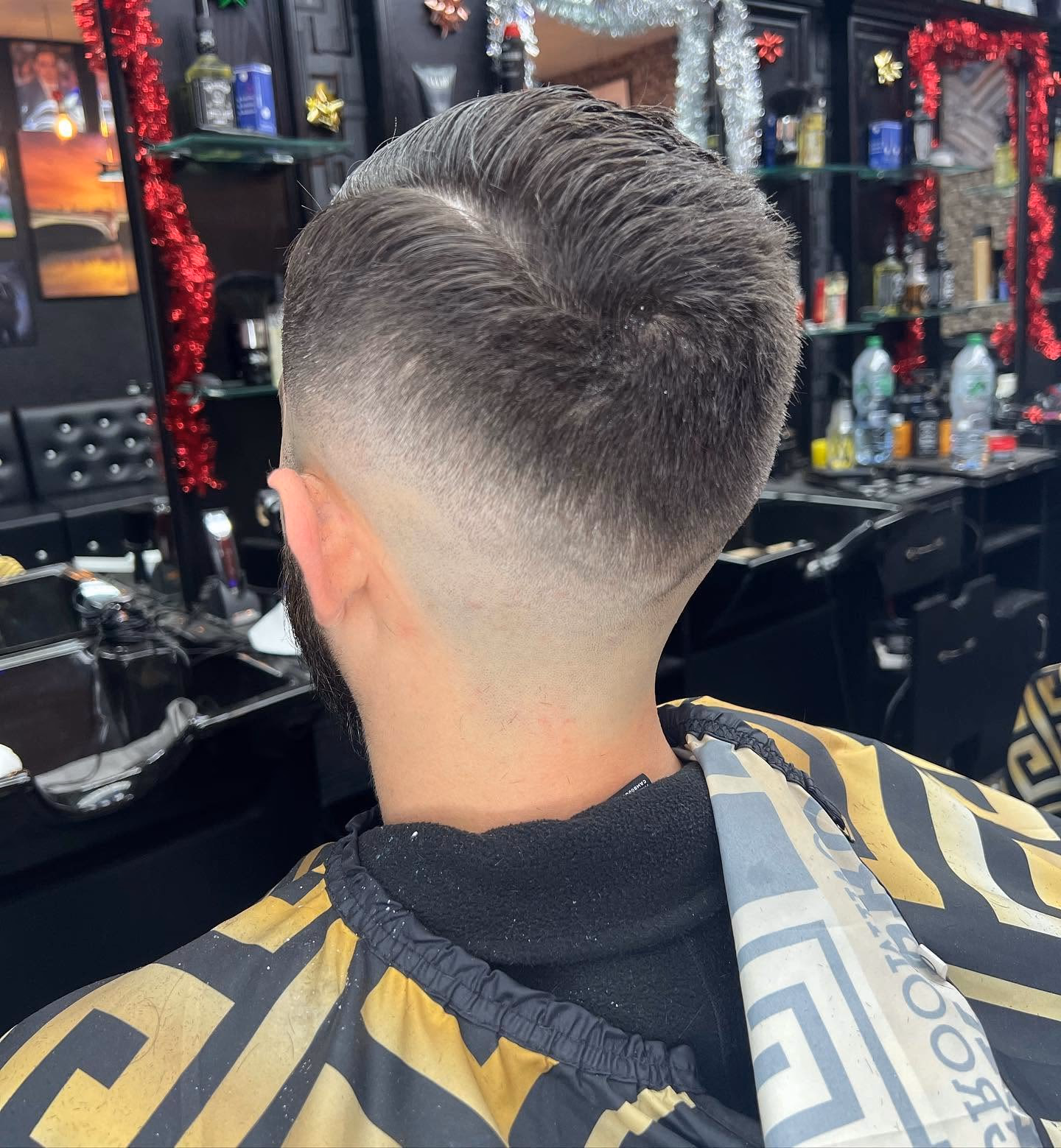 Mid taper fade with a hard shaved side parting and a textured quiff combed over, seen from behind