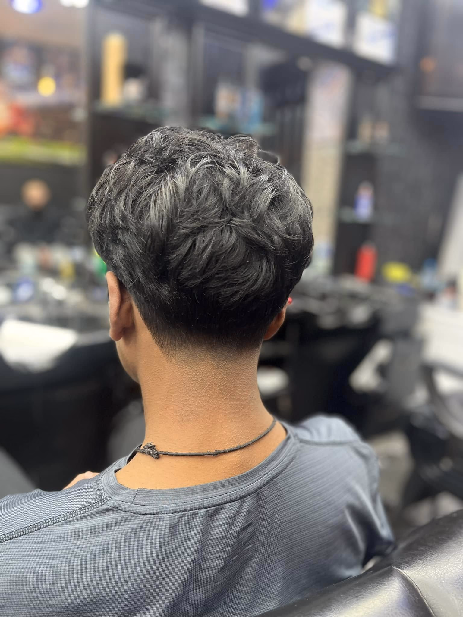 Thick coarse wavy hair left full on top with a clean tapered neckline, seen from directly behind
