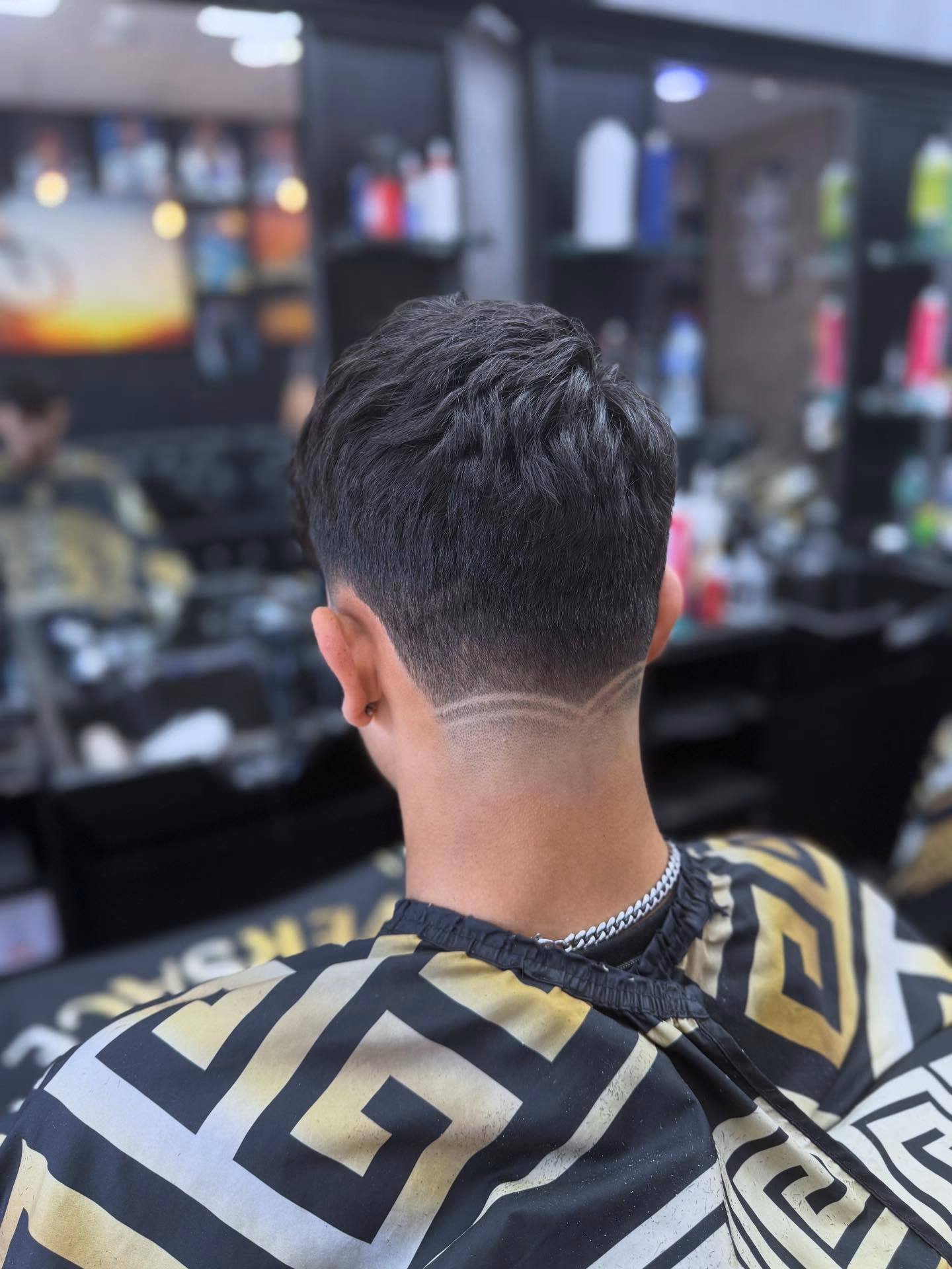 Wavy textured top over a mid fade with a curved line shaved through the back of the fade, seen from behind
